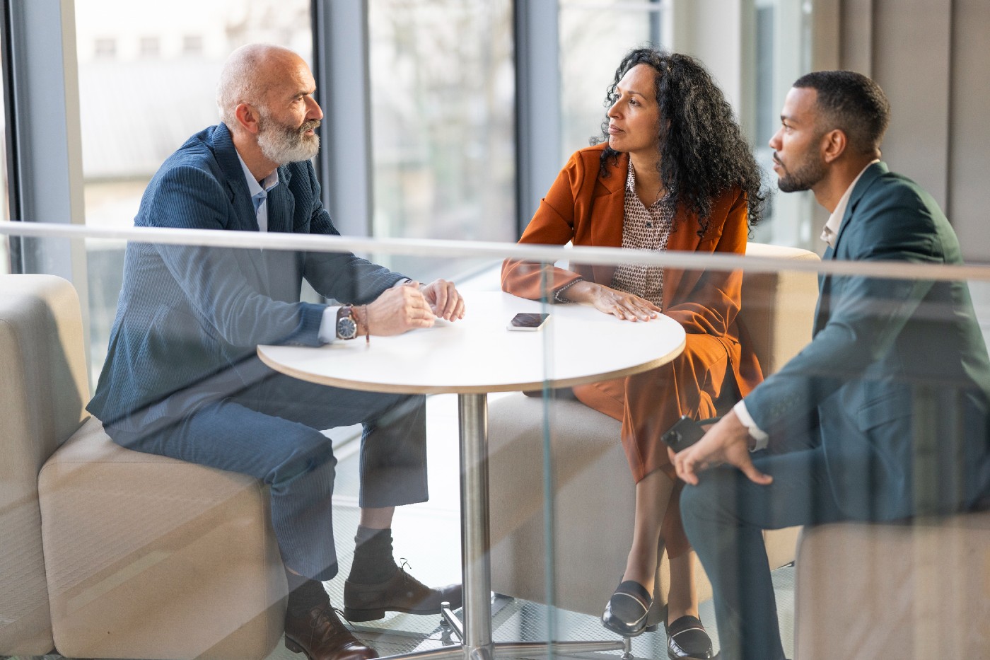 Hispanic female entrepreneur engaging with two investors during a business meeting in a modern office setting with natural light.