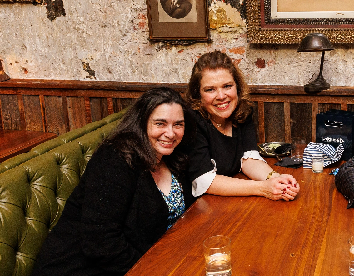 Two women sitting together at a table, smiling.