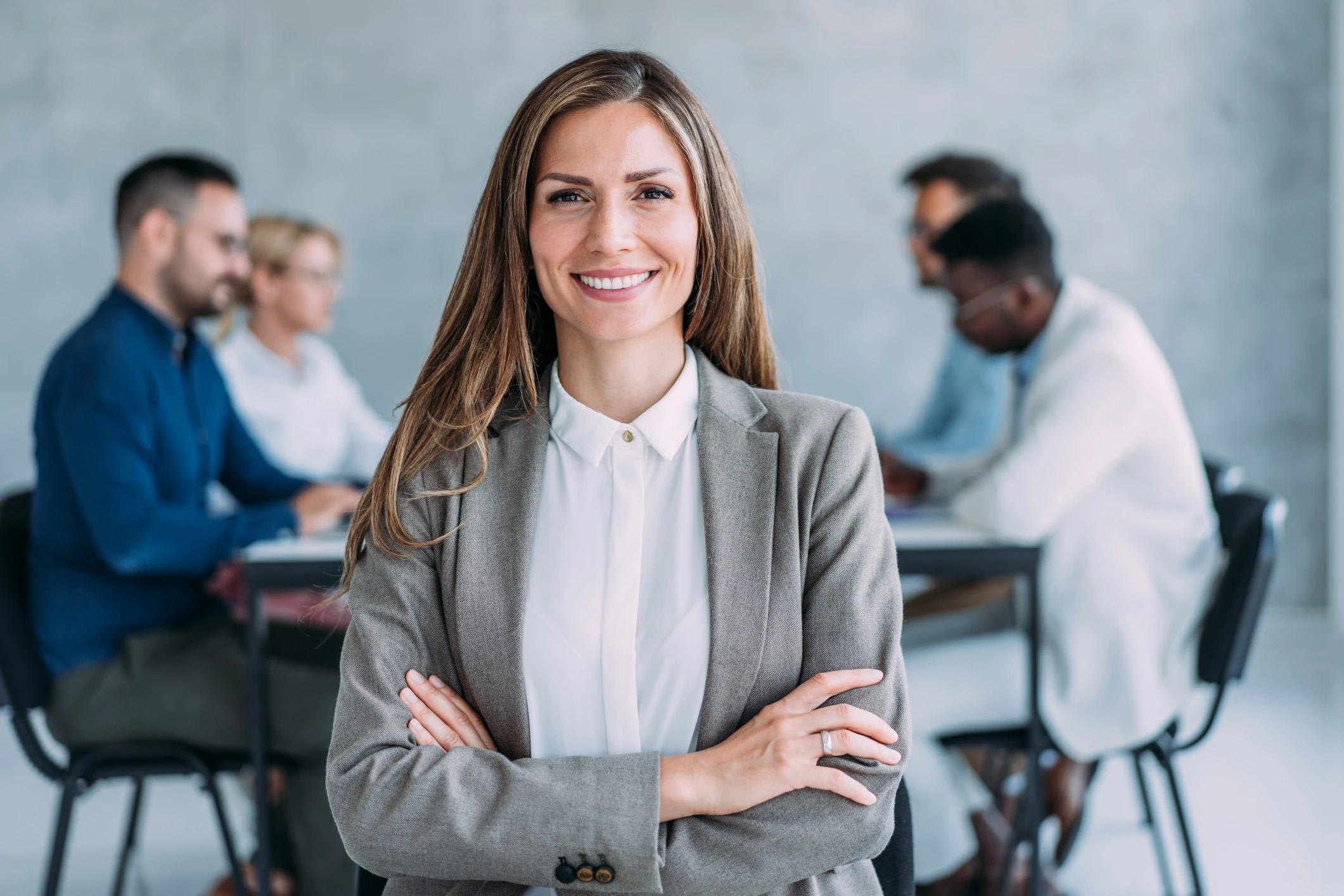 Professional businesswoman standing, smiling at camera with arms crossed.